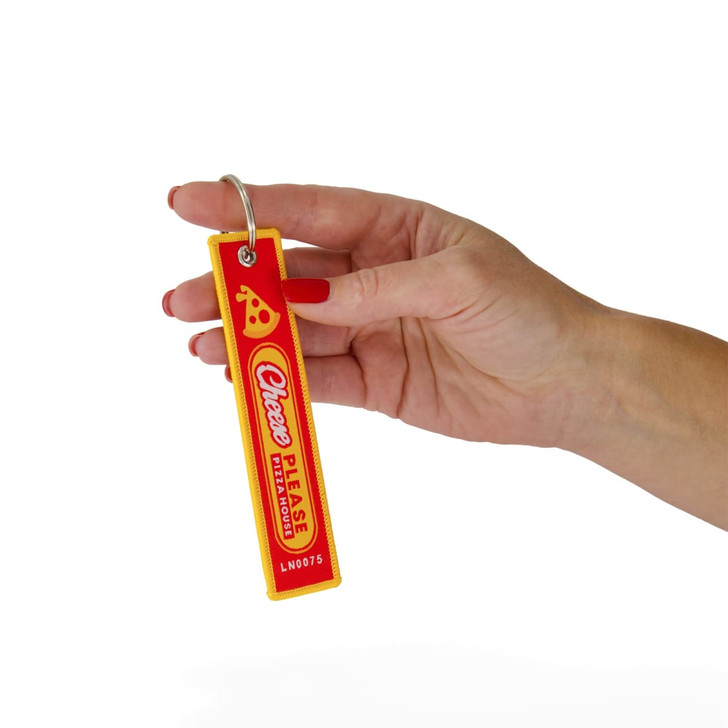 A red and yellow woven keytag featuring a logo, held by a hand with manicured nails.