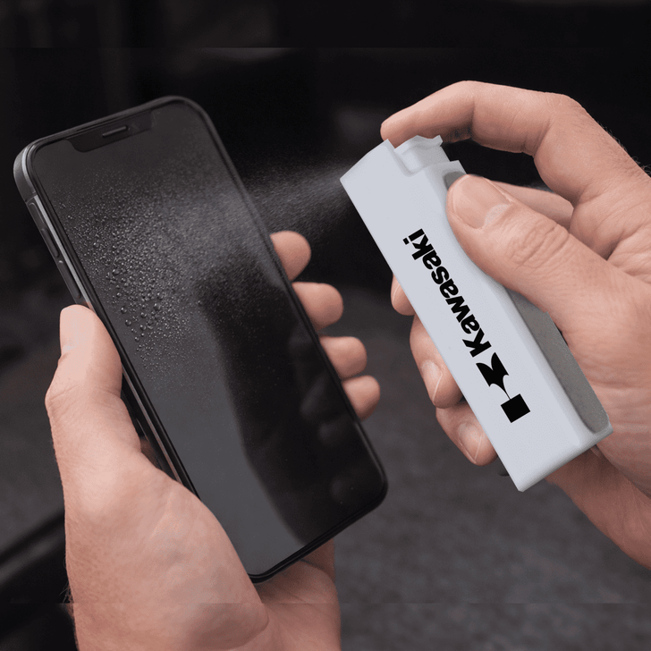 A white spray bottle is cleaning a smartphone screen, which is covered in mist. The bottle has a logo.