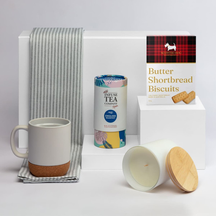 A coffee mug in grey and cork, a tea canister, a candle with a wooden lid, and shortbread biscuits, arranged on a white background.