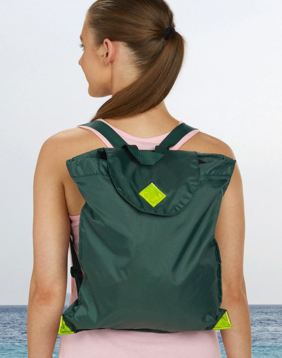 A green excursion bag with a flap and straps worn on the back of a person, set against a beach backdrop.