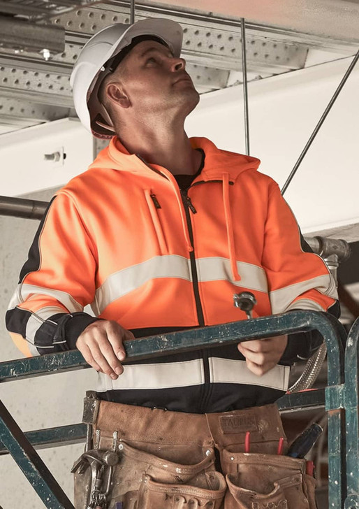 A man wearing an orange and black unisex hi-vis full zip stretch taped hoodie stands on a scaffold, looking upwards.