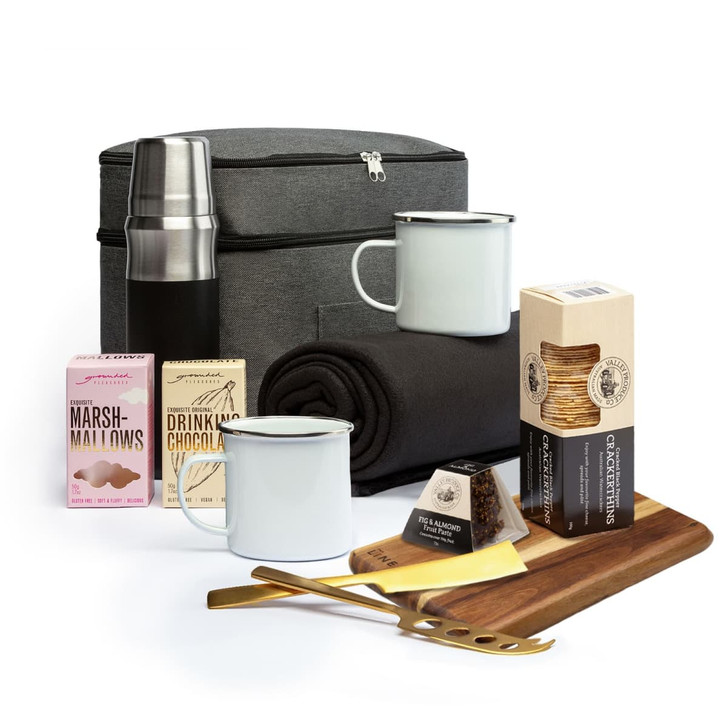 A drink bottle and enamel mugs with marshmallows, drinking chocolate, a blanket, and a cheese board in a storage bag.