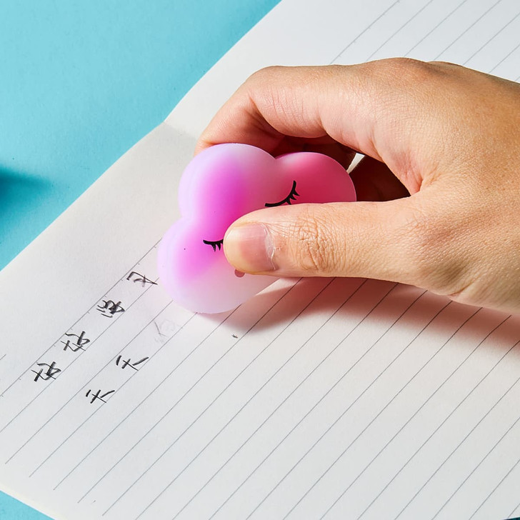 A cloud-shaped rubber eraser in pink and white being used on lined paper, with a hand holding it.