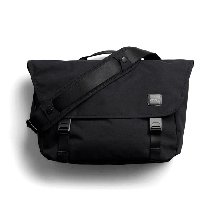 A black messenger bag with a flap, adjustable shoulder strap, and branding label. It features buckle closures and a sleek design.
