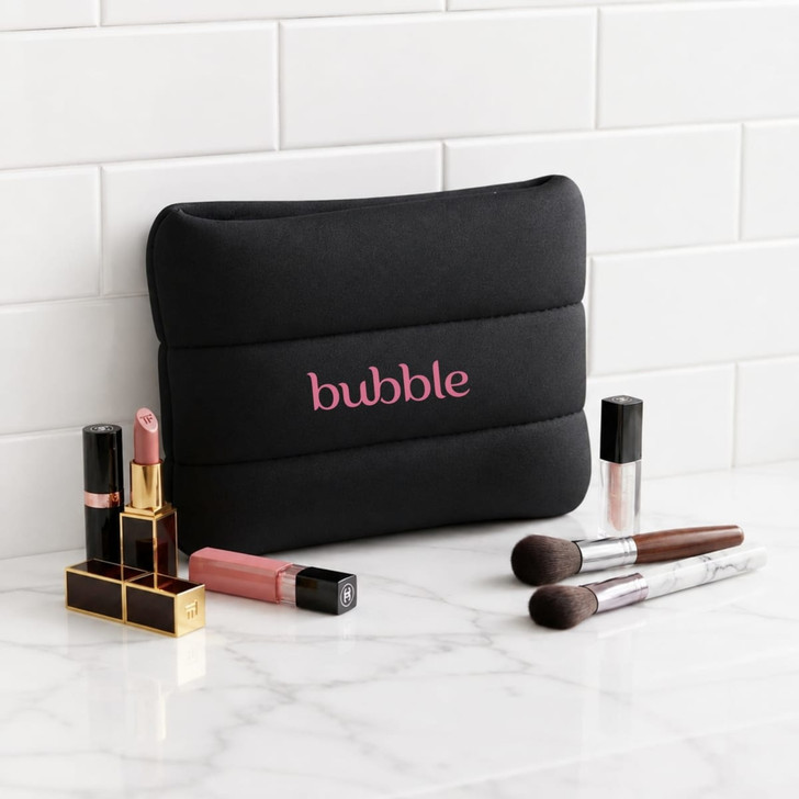 A black neoprene cosmetic bag with pink branding, surrounded by various lip products and makeup brushes.
