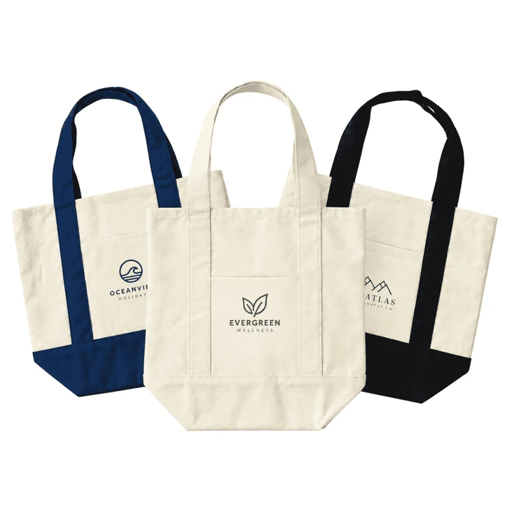 Three mini canvas tote bags in natural, navy blue, and black with various logos on the front.