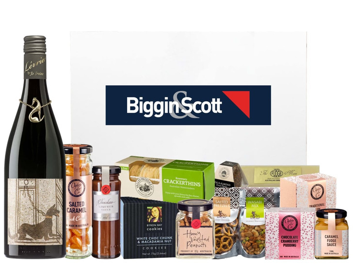A wine bottle, gourmet snacks, cookies, sauces, and sweets in a red and white hamper, featuring a logo.