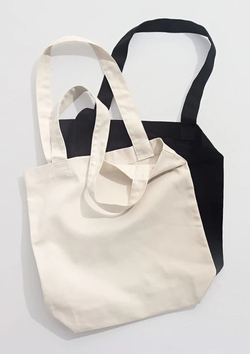 Two canvas tote bags, one in cream and one in black, featuring long handles and a simple design.