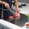 Stainless steel cutting board on a kitchen counter, chef slicing raw meat with knife, ideal for chefs and home cooks, Honesty House brand.