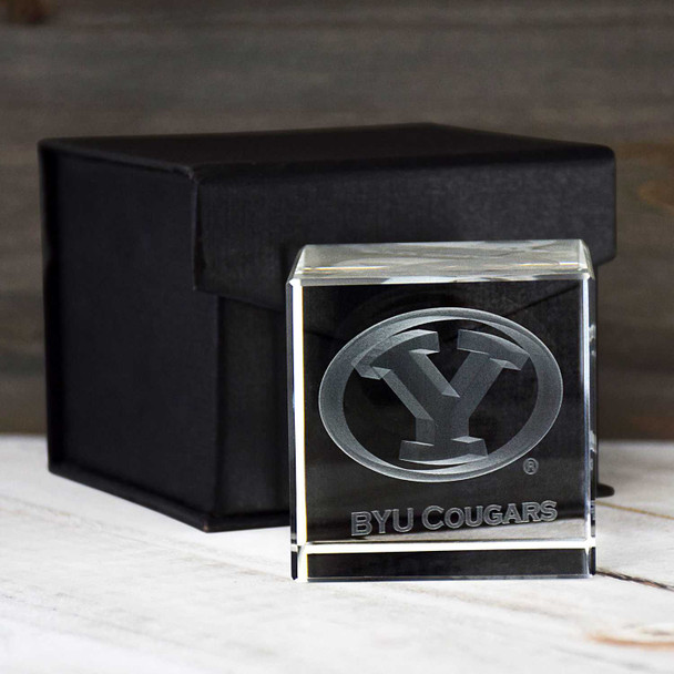 BYU Cougars Crystal Cube, clear glass paperweight with BYU Cougars logo and text, displayed on a white surface next to a black box.