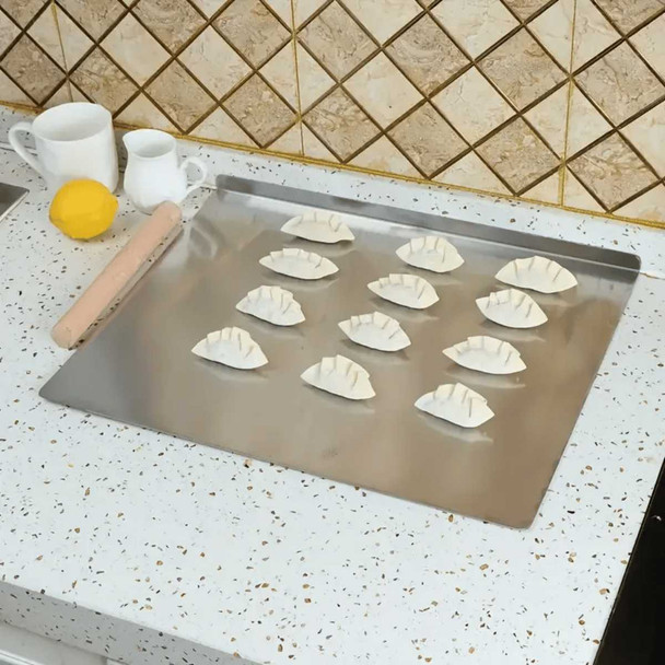 Stainless steel cutting board with lip on kitchen countertop, holding dumplings, rolling pin, and utensils, for food preparation and cooking purposes.