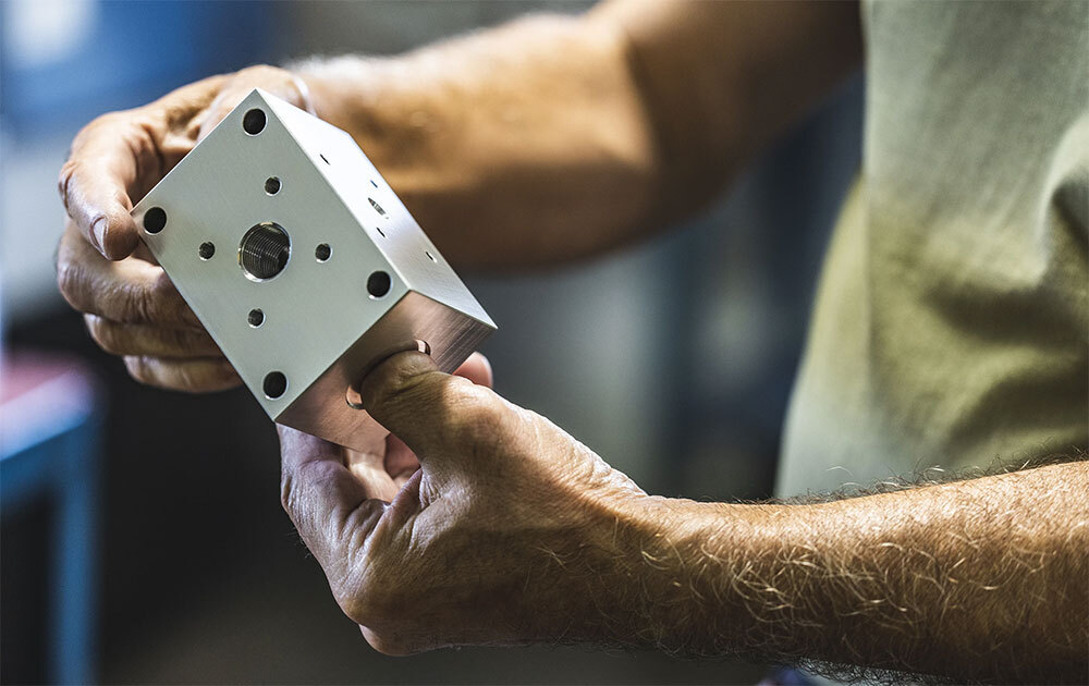 Aerotech CNC machinist inspecting a precision milled aluminum manifold block
