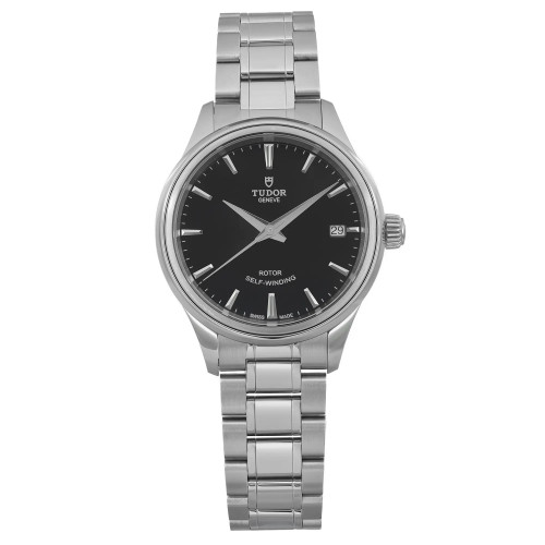 An image of a women's TUDOR Style 34mm wristwatch in an unworn condition, captured from a front-facing angle at a close distance. The watch features a sleek stainless steel bracelet and a black dial with a date indicator at the 3 o'clock position. The watch face includes the brand's logo and "ROTOR SELF-WINDING" text. The watch comes with original box and papers.