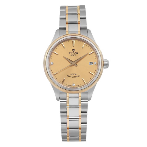 An image of a women's unworn TUDOR Style 34mm wristwatch taken from a front-facing angle at close distance. The watch features a two-tone stainless steel and gold bracelet and a champagne dial with a date indicator located at the 3 o'clock position. The watch hands and hour markers are clearly visible, highlighting the elegant design.