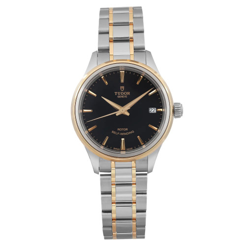 An image of a TUDOR Style 34mm women's wristwatch, displayed from a front-facing angle at a close distance. The watch features a black dial with yellow gold hour markers and hands, along with a date indicator at the 3 o'clock position. The bezel is gold, complementing the two-tone steel and gold bracelet. The watch is in unworn condition.