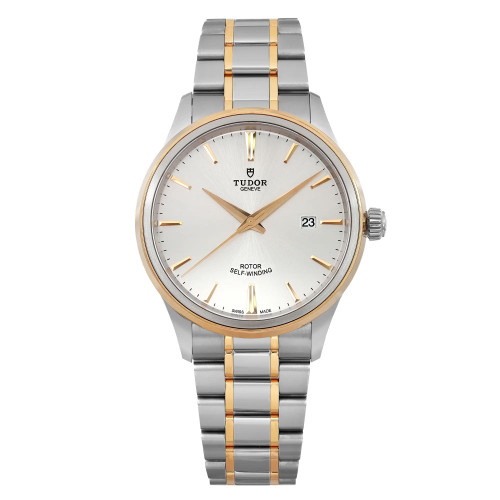 An image of a men's TUDOR Style 41mm wristwatch in unworn condition, featuring a date indicator. The watch is positioned upright, displaying a close-up, frontal view. It has a silver dial with yellow gold hands and markers, and a two-tone metal bracelet with gold and steel links. The watch face is clear and detailed, highlighting the brand name and self-winding rotor feature.