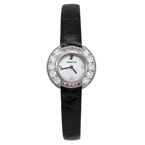 An image of a pre-owned Audemars Piguet women's wristwatch positioned vertically against a plain white background. The watch is viewed from the front, showcasing its round face adorned with sparkling diamonds and a row of pink gemstones. The face features a simple design with black hands and the brand name. The strap is black and made of leather. The image is taken at a close distance, highlighting the intricate details of the watch's design.