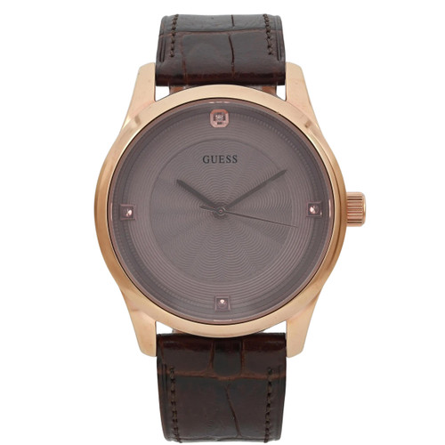 An image of a pre-owned men's GUESS wristwatch. The watch is positioned upright with a frontal view, displaying its round face and gold-tone casing. The dial is a subtle pattern with minimalistic hour markers and hands. The watch has a brown leather strap, textured to resemble alligator skin, and the crown is visible on the right side. The photograph is taken straight-on at a close distance, capturing the details of the watch face and strap.