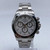 An image of a pre-owned men's Rolex Daytona Stainless Steel White Index Dial Automatic Men Watch 116520 positioned upright on a stand, captured from a frontal angle at a moderate distance. The watch features a chronograph with three subdials, luminous hands, and a small seconds subdial, set against a polished metal bracelet.