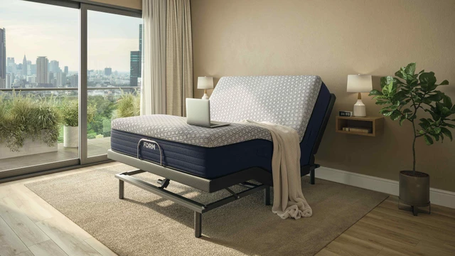 Person working on a laptop in bed with the FORM Adjustable Bed Base raised to a lounge position