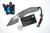 Full product layout of Microtech Stitch RAM-LOK knife with extras including challenge coin, PVC patch, and lanyard bead.