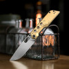 Lifestyle image of brass Artisan Beest knife displayed on tabletop near lantern