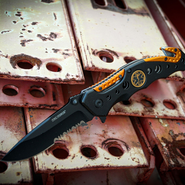 Tac-Force TF-723EM EMS rescue folding knife displayed open on industrial steel beams, highlighting the assisted opening blade, emergency rescue tools, and black and orange aluminum handle.