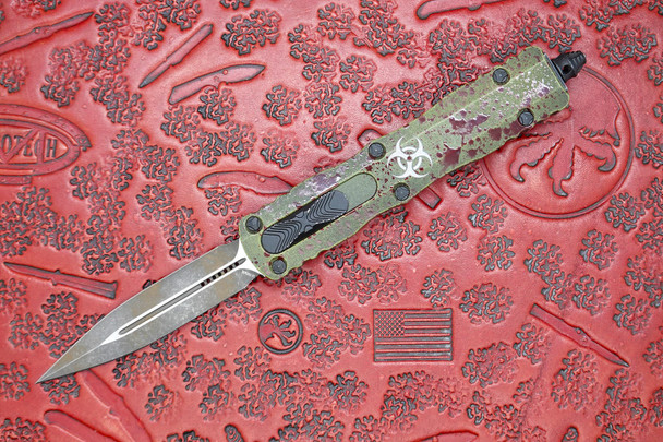 Open view of the Microtech Dirac 225-1OBDS Outbreak Signature Series showing distressed M390 dagger blade and distressed green aluminum handle with biohazard logo.