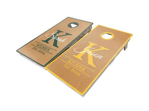A set of cornhole boards featuring a personalized monogram and family name design with an established date. The boards showcase a rich woodgrain finish with contrasting trim in green and yellow. The boards highlight their high-quality construction and precision detailing, making them perfect for outdoor events, backyard gatherings, and weddings.