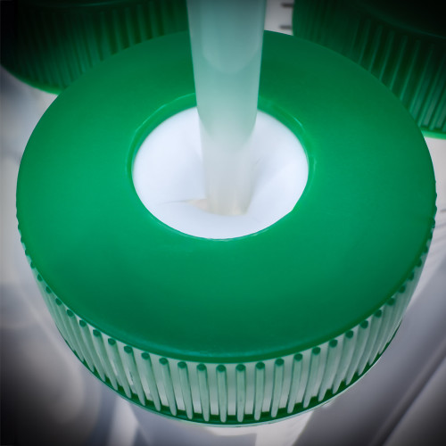 A pipette tip dispensing liquid through the cross-cut septum of a green SeptaSecure centrifuge tube cap. This cap is specifically engineered to provide contamination-free entry for precise liquid handling in laboratory settings, enhancing efficiency and accuracy.