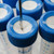 Type-F tubes capped with a blue, cross-cut septum. The septum in one of the caps is punctured by a needle, likely for the purpose of withdrawing or adding fluids without contaminating the contents. The sides of the tubes are marked with measurements and are partially filled with an unidentified liquid