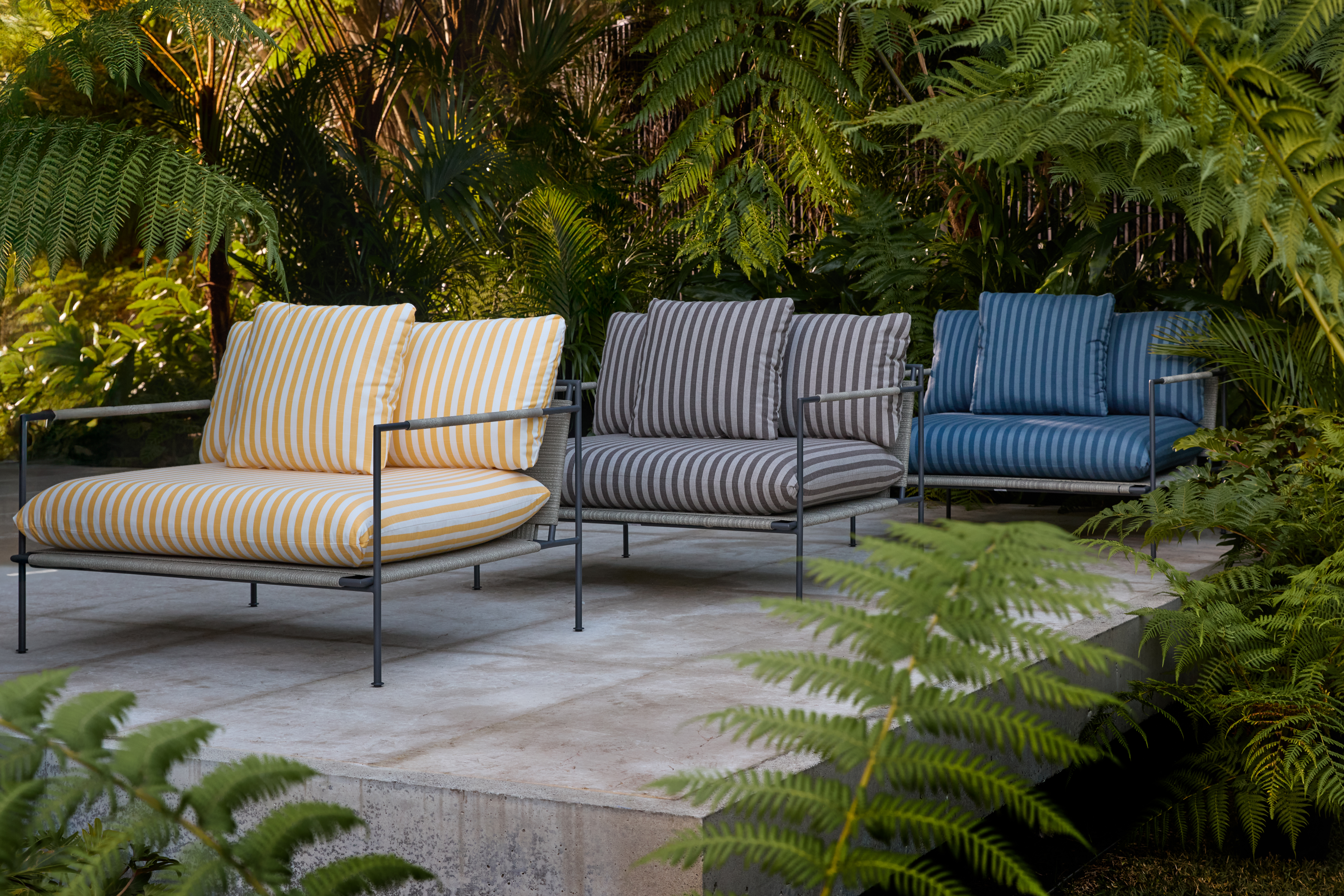 An elegant sheltered space showcasing a low‑slung lounge chair in striped upholstery, its minimal form and soft cushions placed against a window with gridded panes and a nearby potted plant—suggesting a tranquil Japandi-inspired retreat.