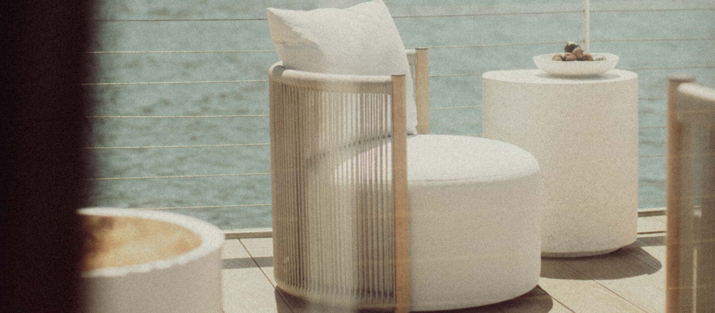 A teak outdoor swivel chair with white cushions against a backdrop of the ocean