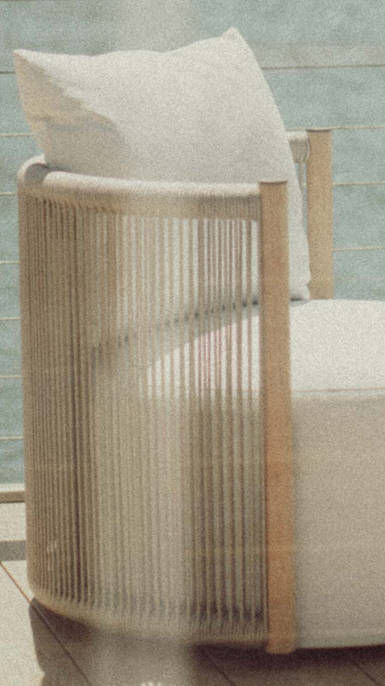A teak outdoor swivel chair with white cushions against a backdrop of the ocean