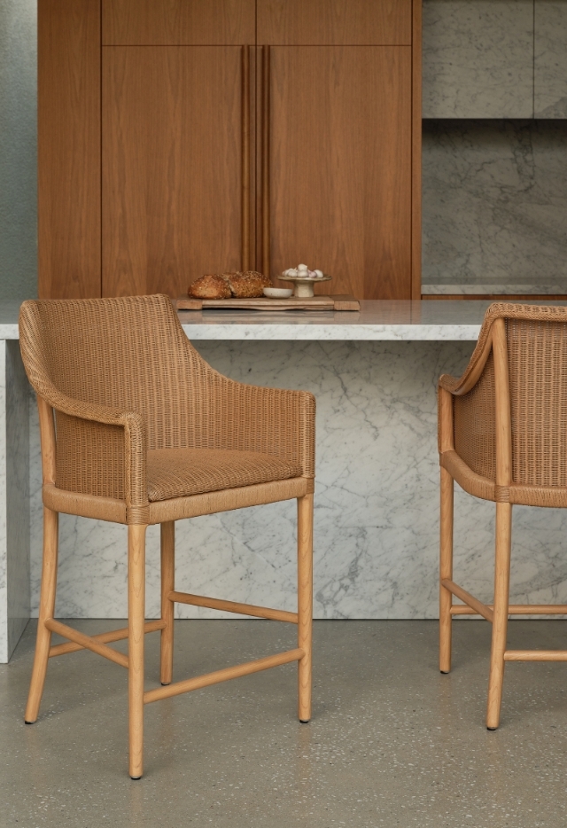 A light-colored Laguna Counter Stool with woven detailing and a natural wood frame sits at a white marble kitchen counter.