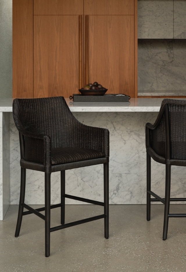 A dark Laguna Counter Stool with woven detailing and a dark frame sits at a white marble kitchen counter.
