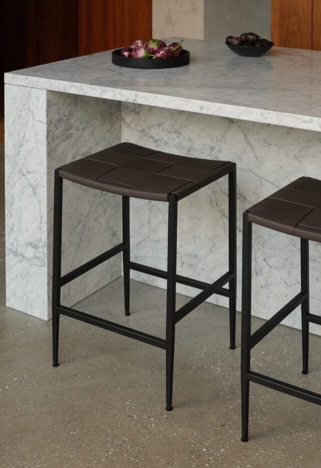 A Madrid Counter Stool with a dark woven leather seat and a black frame sits at a white marble kitchen counter.