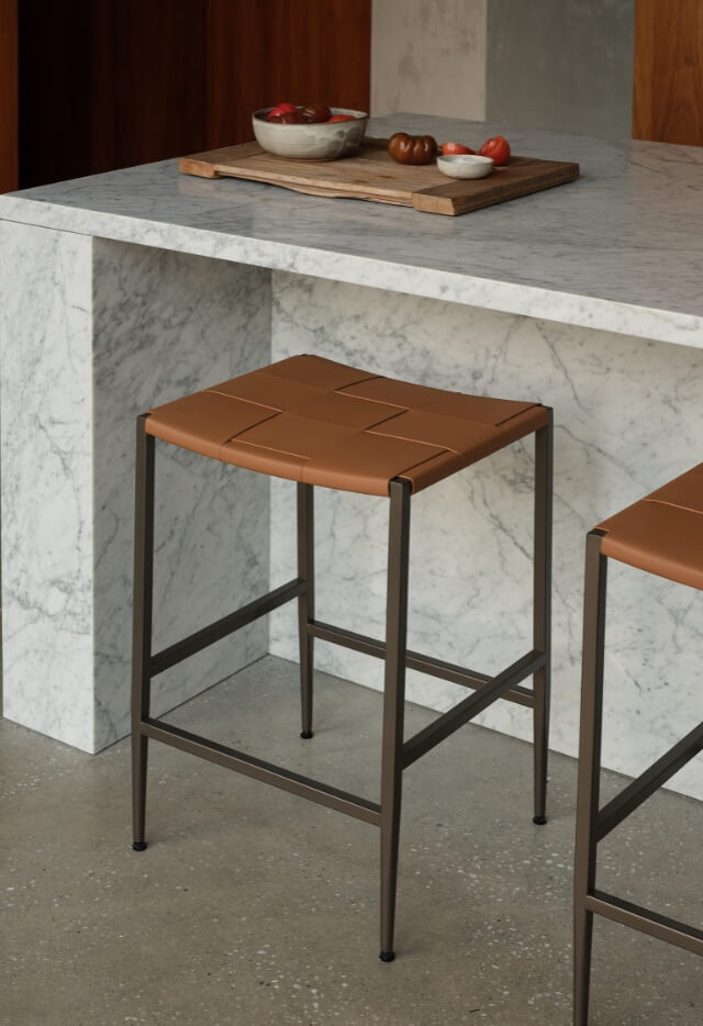 A Madrid Counter Stool with a brown woven leather seat and a black frame sits at a white marble kitchen counter.