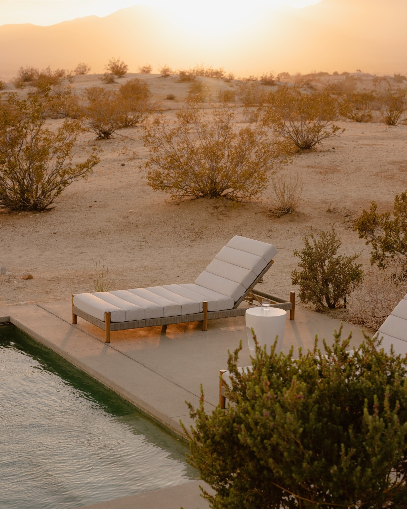 Outdoor sun lounge with upholstered cushions and teak frames, positioned poolside in a desert landscape.