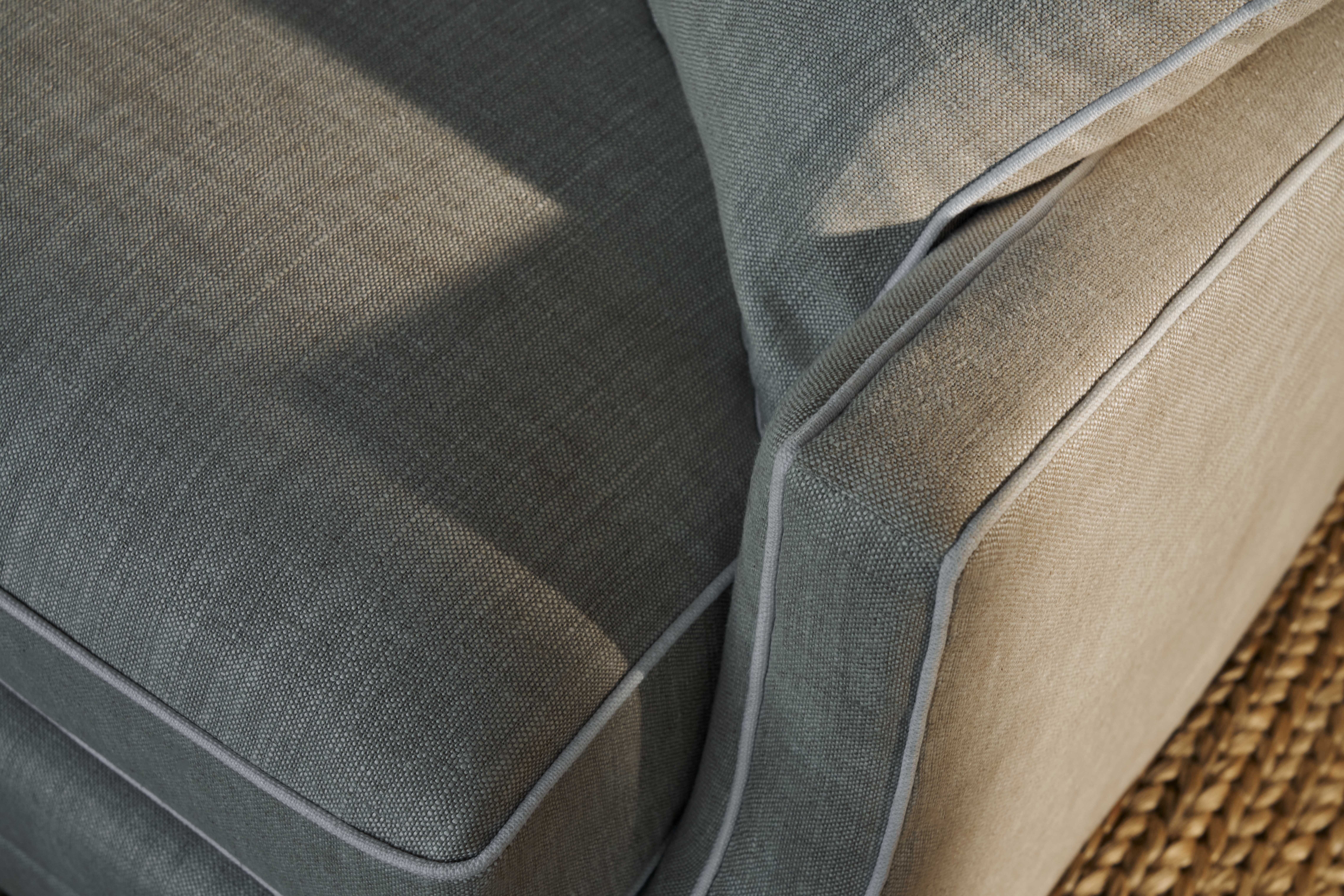Close-up of Coco Republic Ashley Sofa showcasing tailored piping and textured grey linen upholstery in natural light.