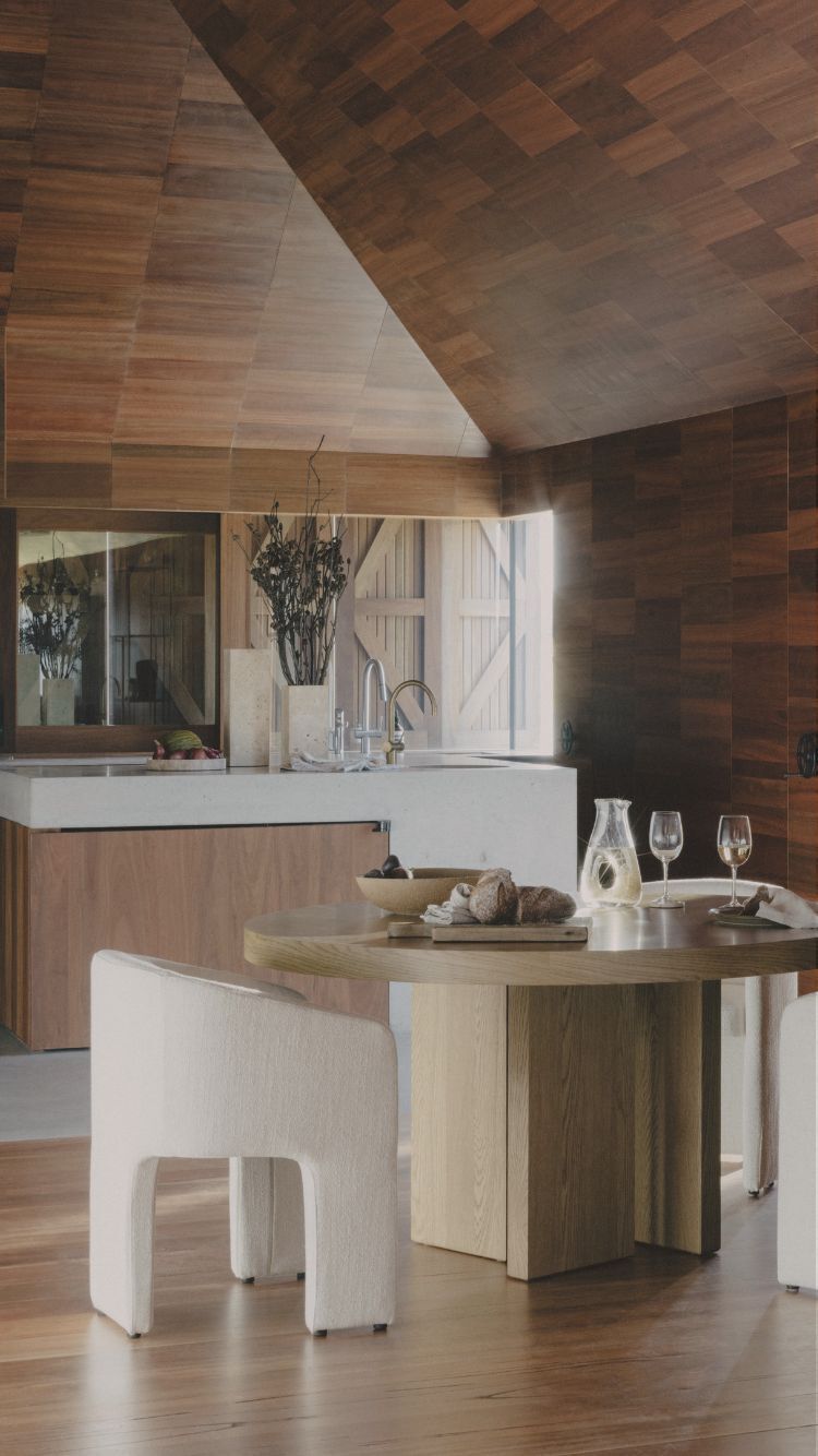 A round timber dining table with white fabric dining chairs