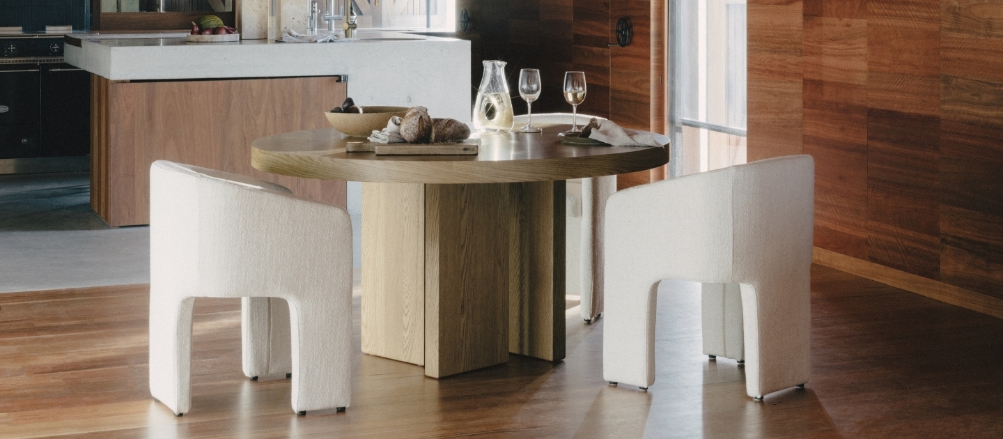 A round timber dining table with white fabric dining chairs