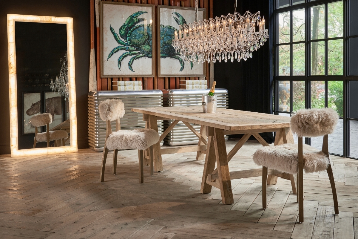 Rustic dining setting featuring Cabin Dining Chairs upholstered in New Zealand sheepskin with weathered oak frames, styled beneath a crystal chandelier.
