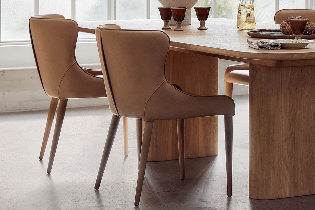 Dining setting featuring six Markson Dining Chairs in tan vegan leather around a natural timber table, styled with glassware and ceramics.