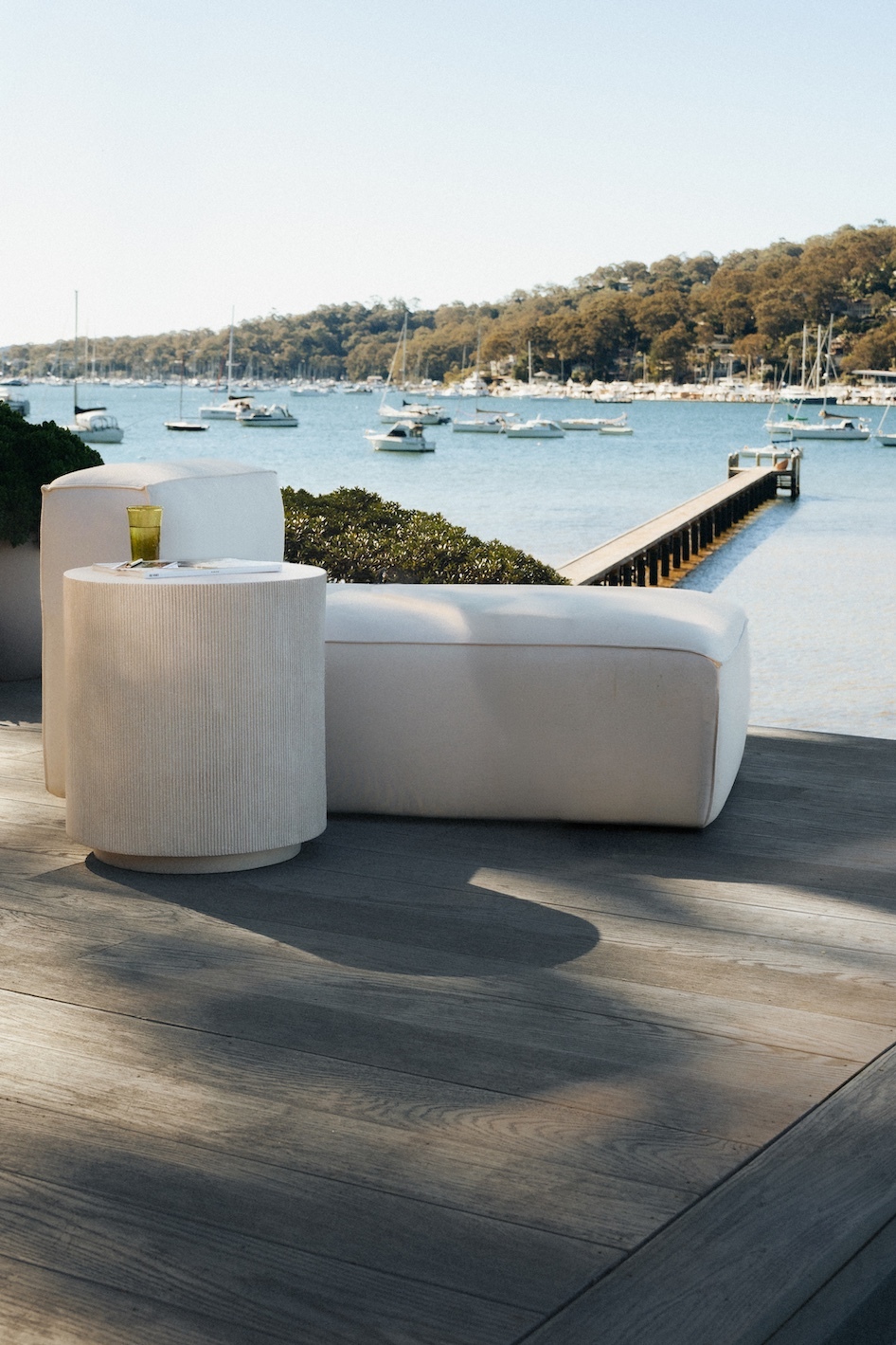 Sculptural white outdoor lounge and side table on a timber deck overlooking the harbour