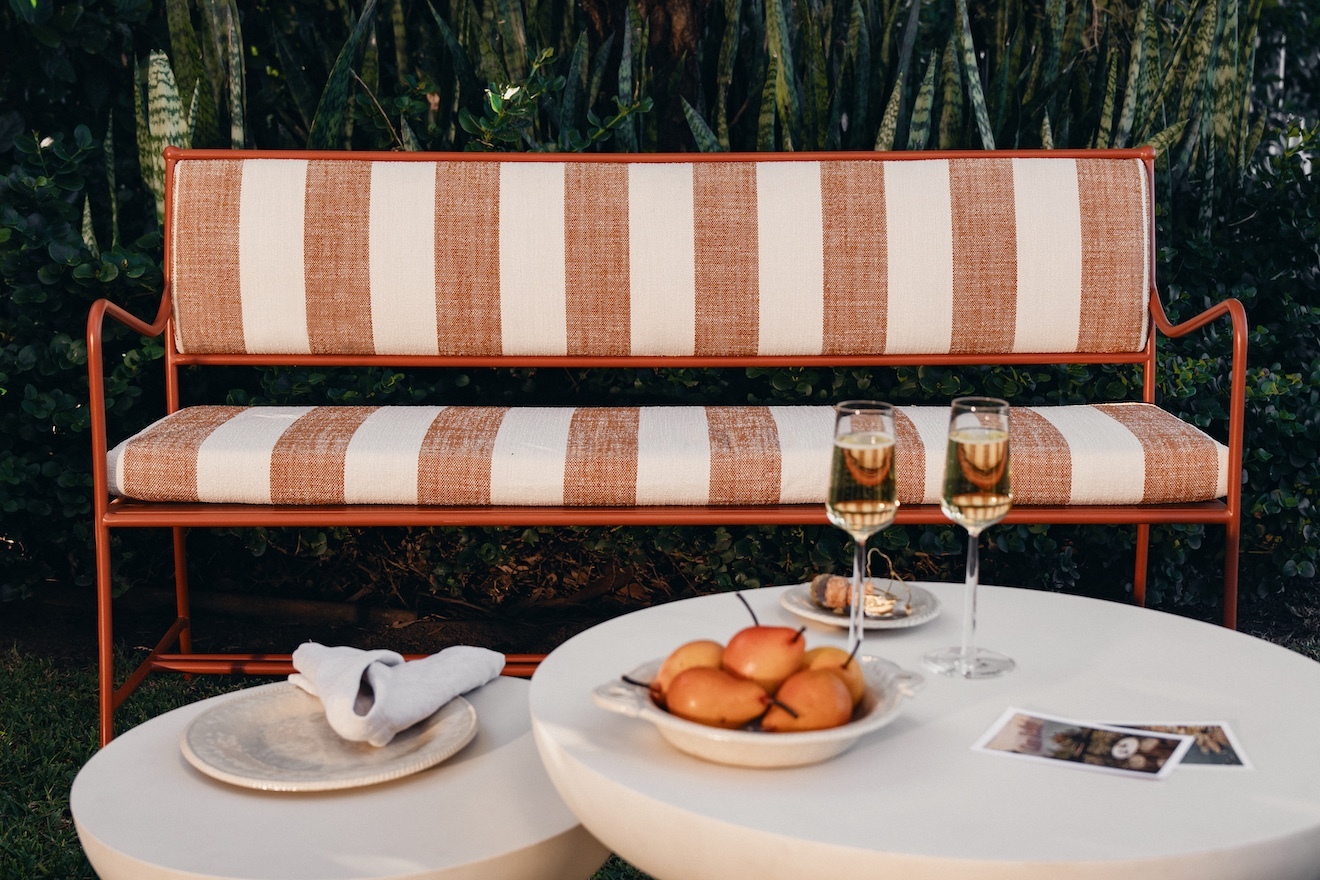 Striped outdoor bench beside a round table set with glasses and pastries in the garden