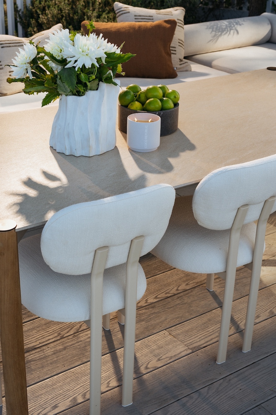 Timber outdoor dining table set with white flowers and cream upholstered chairs