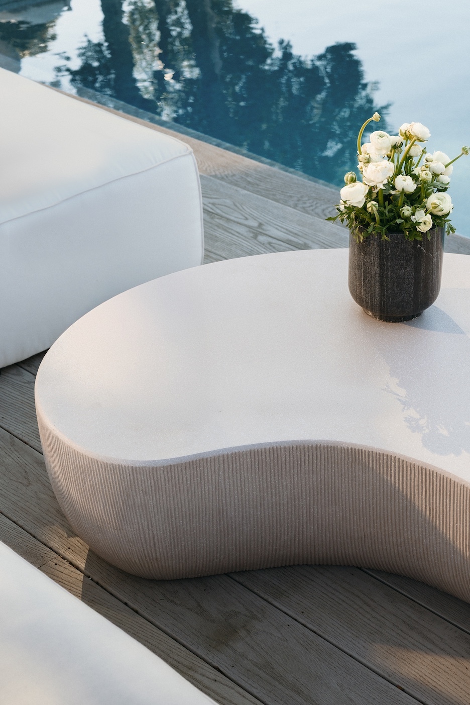 Curved white coffee table with a vase of white flowers beside the pool