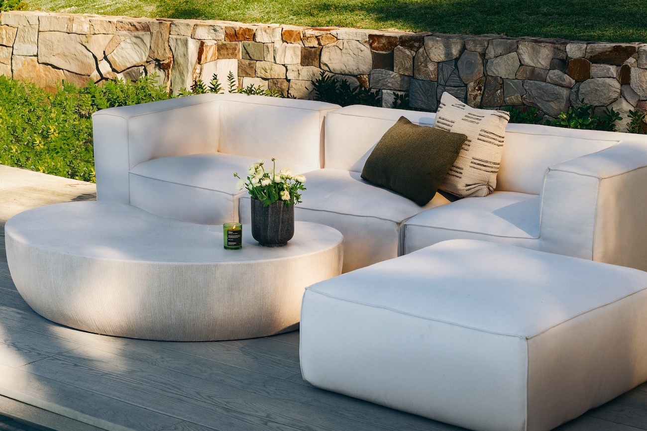Curved white outdoor sofa with striped cushions against a sandstone garden wall