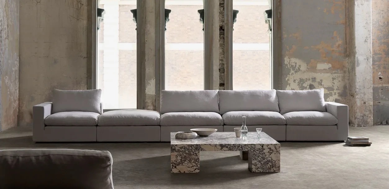 Dune Square Arm Modular Sofa in grey linen, styled against raw concrete walls with a sculptural marble coffee table